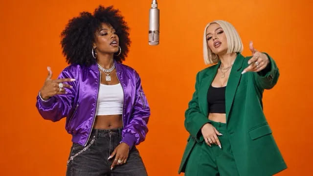 Two women in colorful jackets rapping in an orange booth